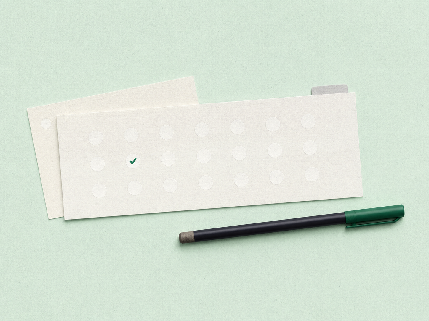 A class roster strip on a mint desk with twenty-three quiet dots and a single forest-green check marking the day’s one absence